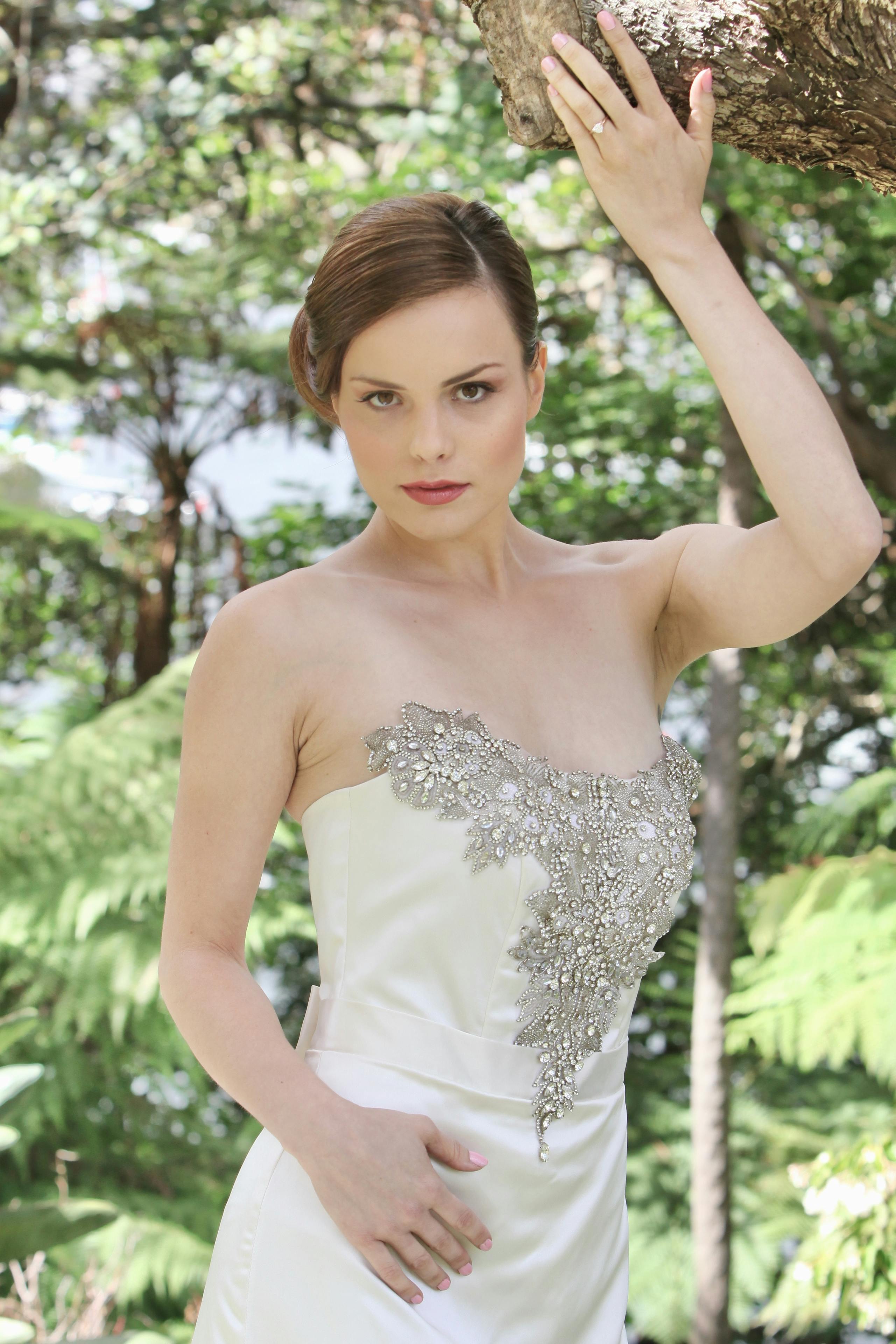 Beautiful bride posing elegantly in a park setting, showcasing a detailed wedding gown.