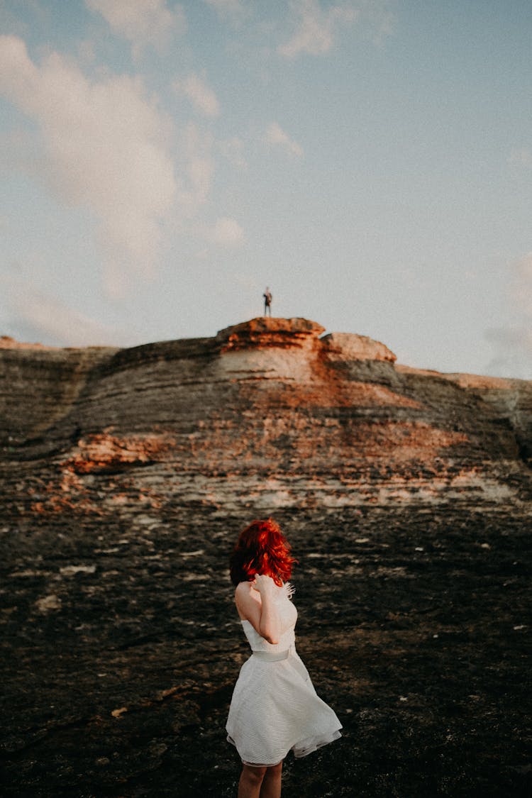 Redhead In Dress Looking At Person On Top Of Mountain