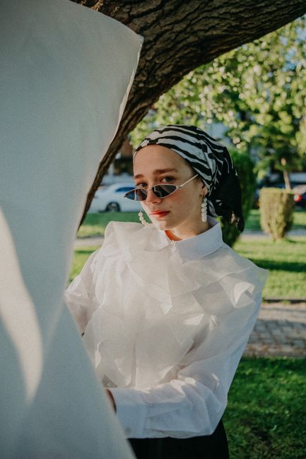Elegant woman wearing sunglasses and headscarf in a stylish outdoor portrait during the day.