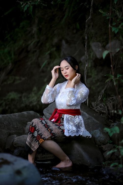 Free Asian woman in traditional attire sitting by a stream, exuding elegance and serenity. Stock Photo