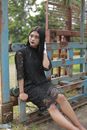 Woman in Black Floral Dress Sitting on Brown Wooden Fence