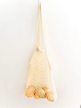 A reusable mesh bag filled with fresh yellow fruits hanging against a white wall.
