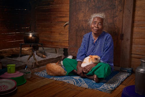 Woman With White Hair In Blue Long-sleeved Top Sitting With White And Orange Tabby Cat