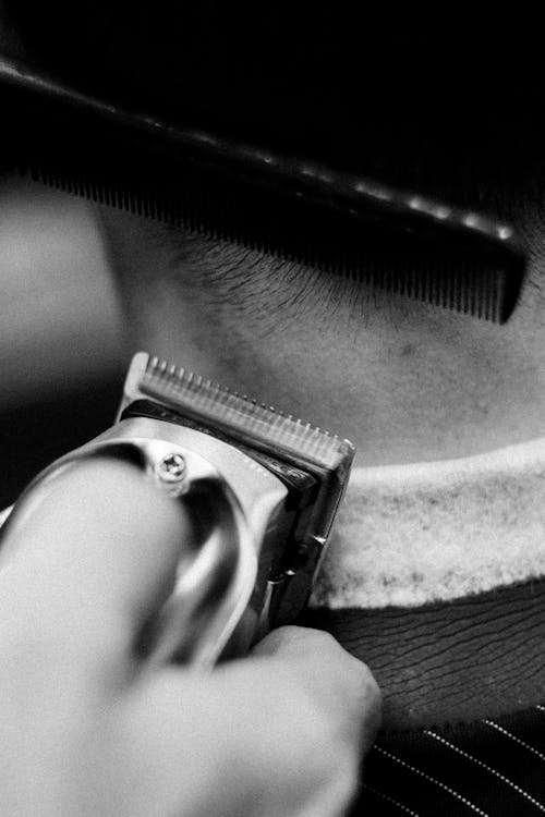 Grayscale Photo of Person Holding a Comb and a Razor to Cut a Someone's Hair