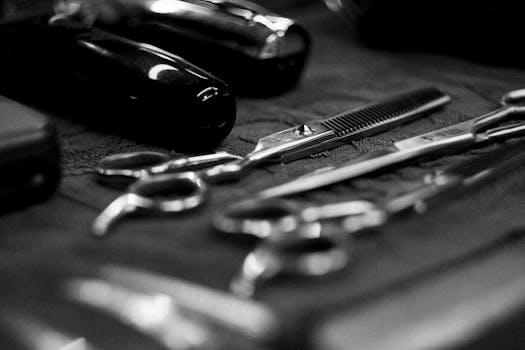 Monochrome close-up of various barber tools including scissors and clippers on a textured surface.