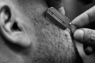 Detailed black and white image of a man shaving with a straight razor, showing texture and technique.