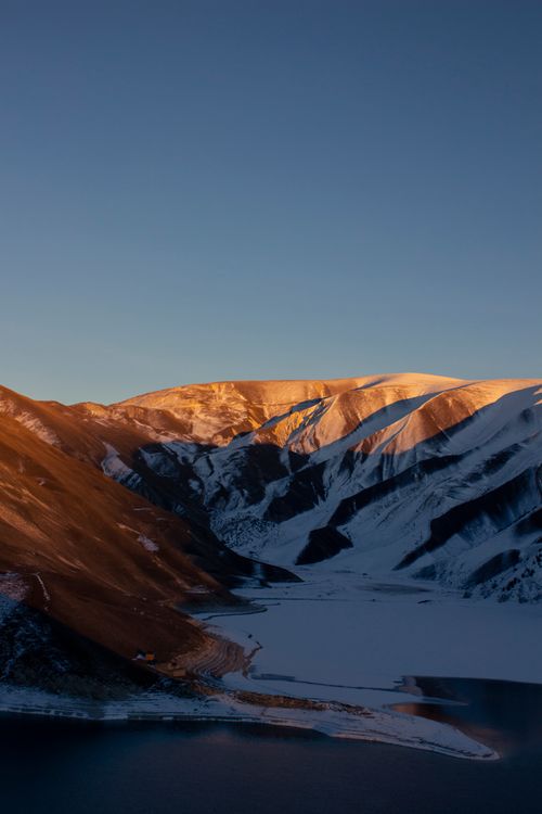 Free Beautiful sunrise illuminating a snow-capped mountain range reflected in a serene lake. Stock Photo
