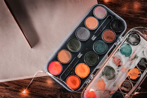 Free Artistic close-up of a watercolor paint palette with vibrant, warm hues on a wooden surface. Stock Photo