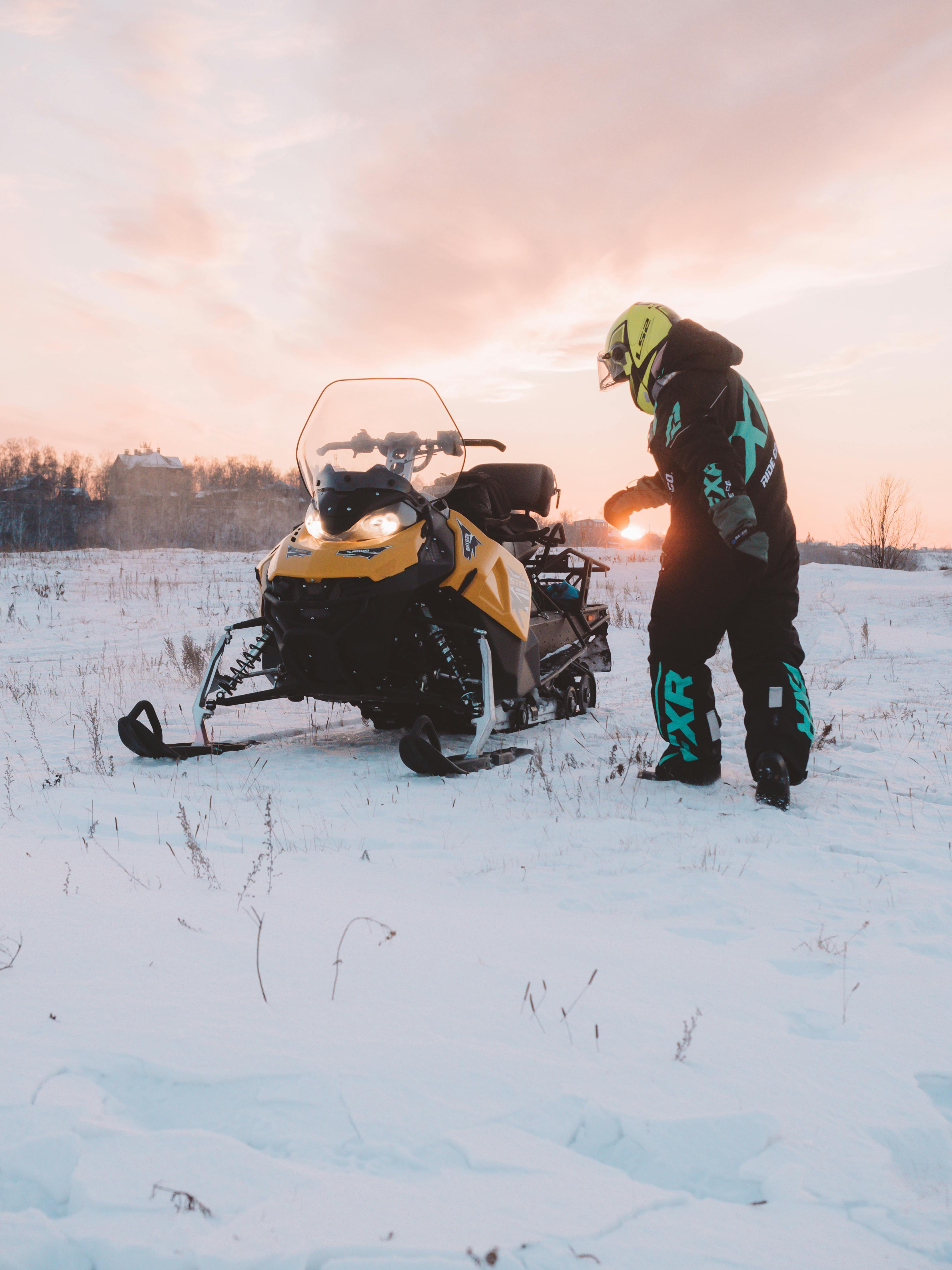 man in overalls with snow bike and pastel pink sky