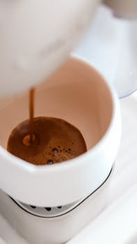 A rich espresso coffee pouring into a white cup from a coffee machine.