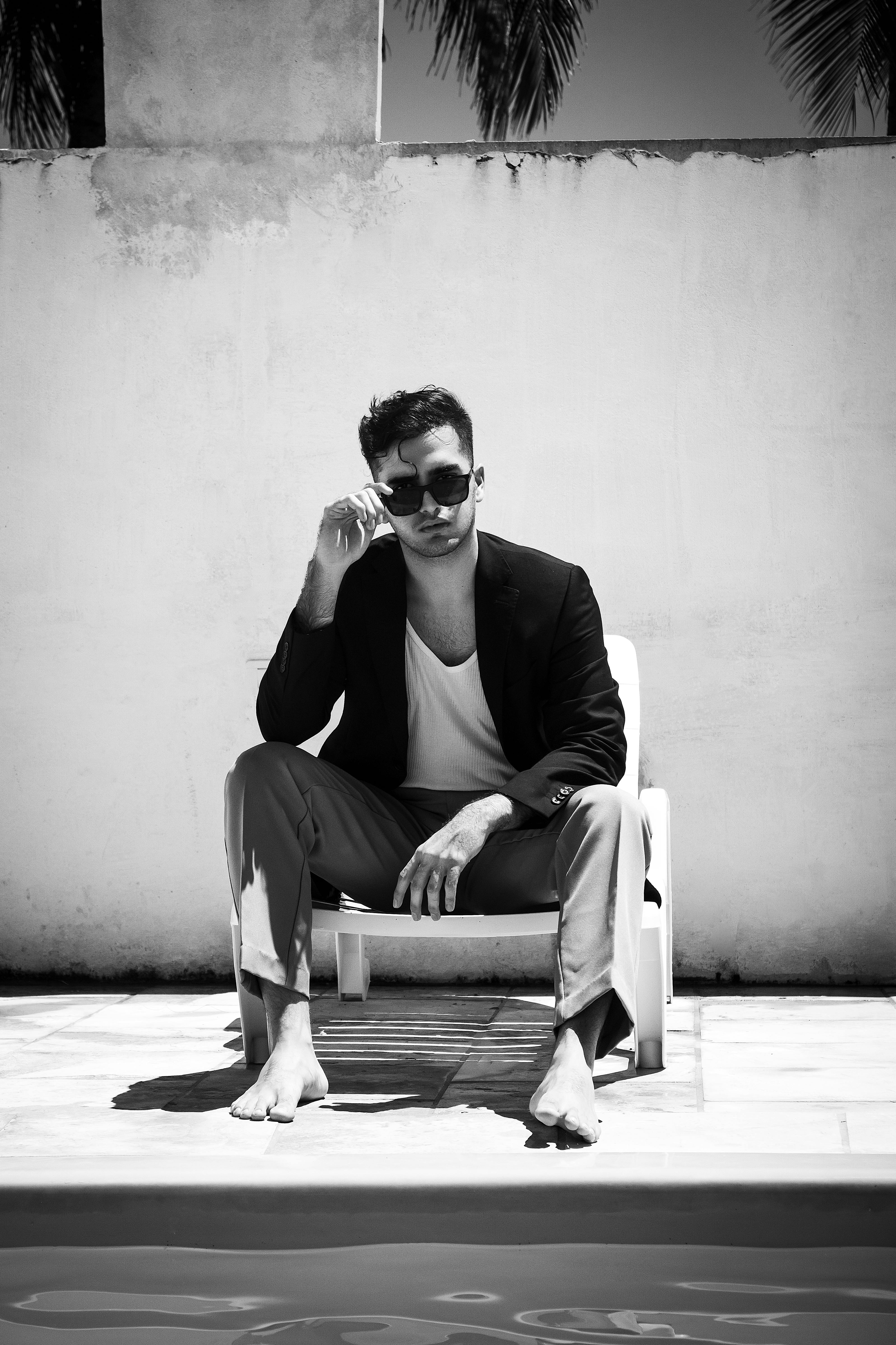 Sophisticated black and white photo of a man relaxing by the pool in sunglasses and a blazer.