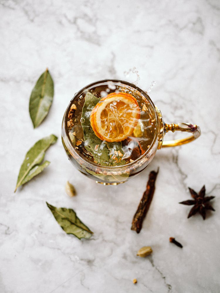 A Cup Of Tea With Herbs Lying Next To It