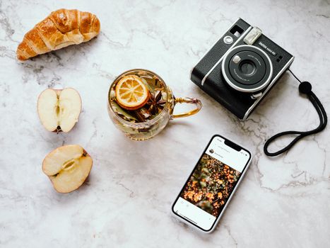 An elegant flat lay featuring tea, a croissant, an instant camera, and a smartphone on a marble surface.. elegant, flat, feat