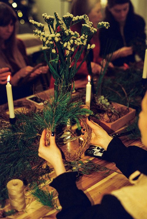Free A cozy indoor scene with women making festive wreaths, surrounded by candles and greenery. Stock Photo