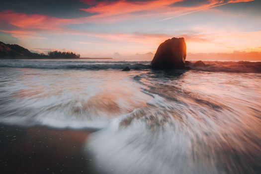 Stunning seascape with flowing waves and a rocky shoreline at sunset, capturing nature's beauty.