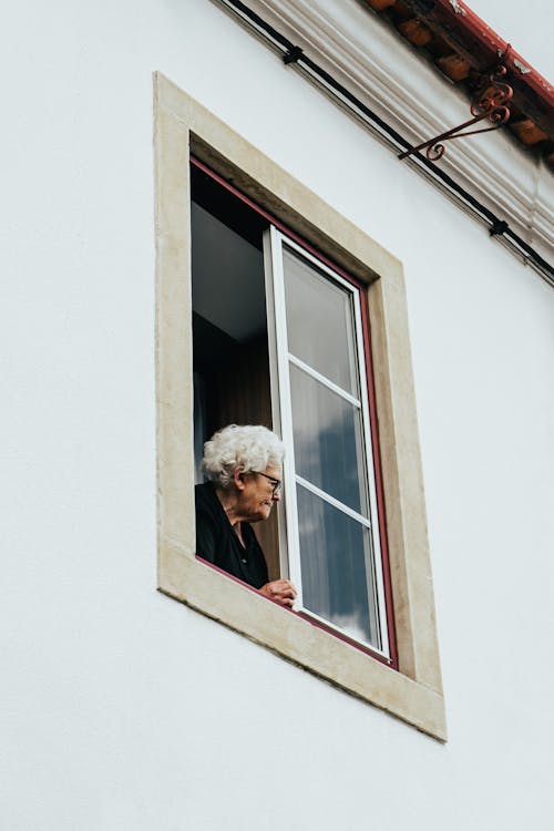 Ảnh Chụp ở Góc Thấp Của Một Người Phụ Nữ Lớn Tuổi Nhìn Ra Ngoài Cửa Sổ