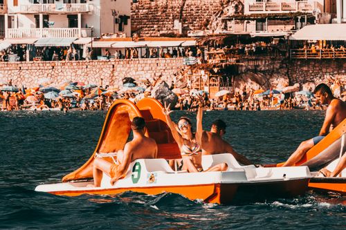 Free Tourists enjoying a sunny day riding pedalos on the coast of Montenegro with a lively beach in the background. Stock Photo