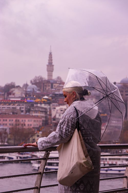 Free A woman holding a clear umbrella overlooking Istanbul's skyline in the rain. Stock Photo