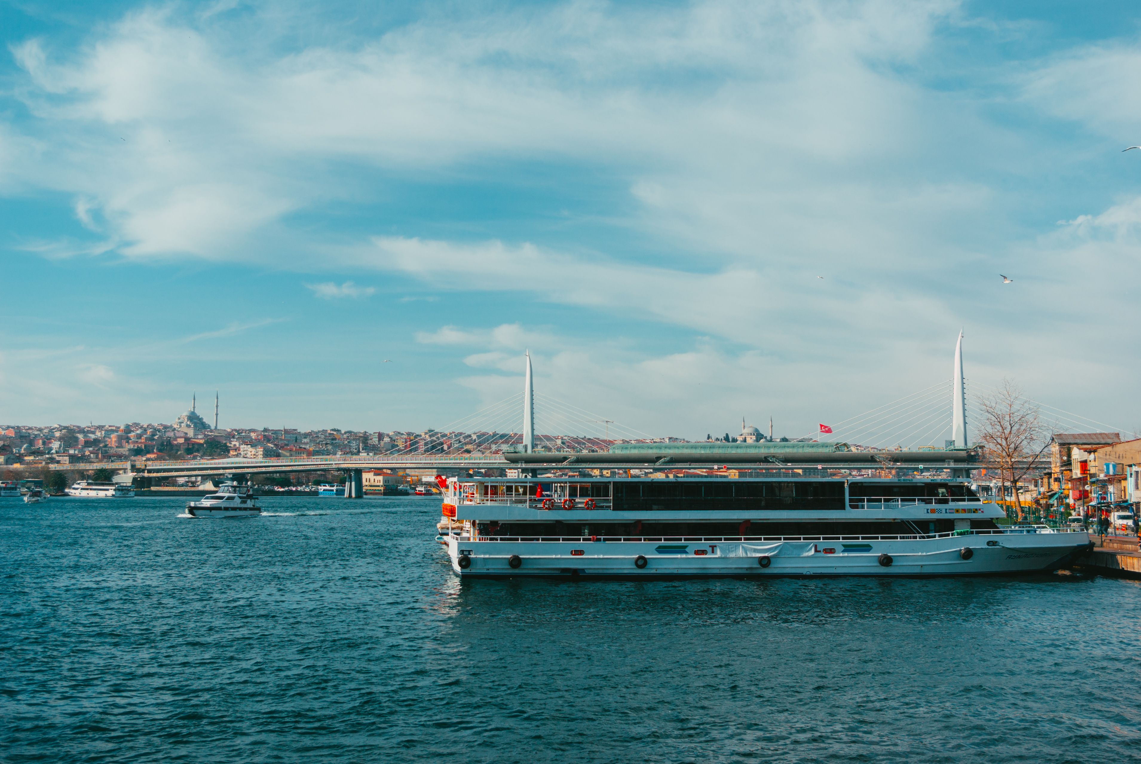 A tranquil scene of a ferry on the Bosphorus with view of Halic Bridge in Istanbul under blue skies.