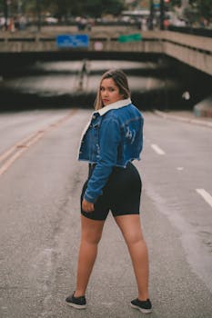 Confident woman in denim jacket standing on city street looking back.
