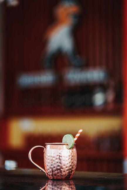 A copper mug filled with an Irish Mule cocktail, garnished with a lime wheel and crystallized ginger, condensation beading on the metal.