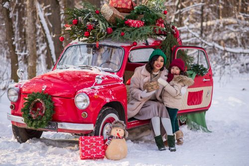 Free Mother and daughter in warm clothing enjoy a snowy festive scene with a decorated red vintage car. Stock Photo