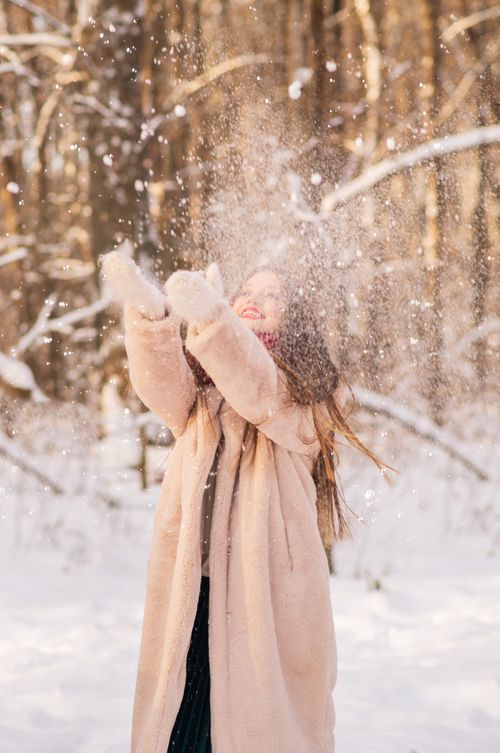 Free Woman in a coat throwing snow in a snowy forest, embracing winter joy. Stock Photo