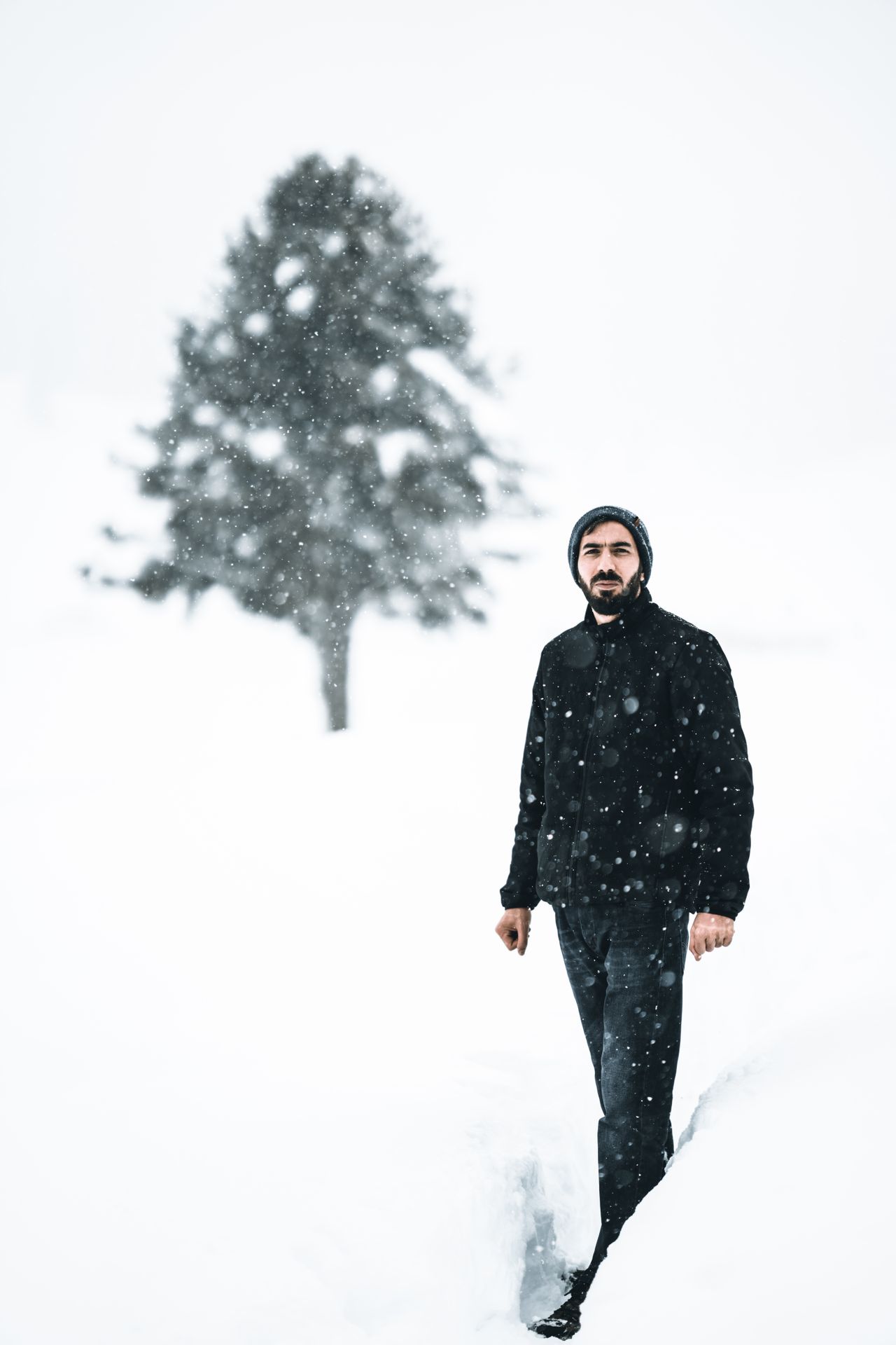 Man in a black winter outfit walking through falling snow