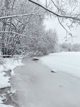 A tranquil winter scene with a frozen river bordered by bare, snow-laden trees.