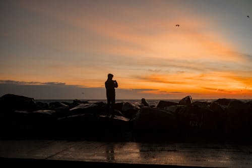 Silhouette of Man Standing on Big Rocks during Sunset