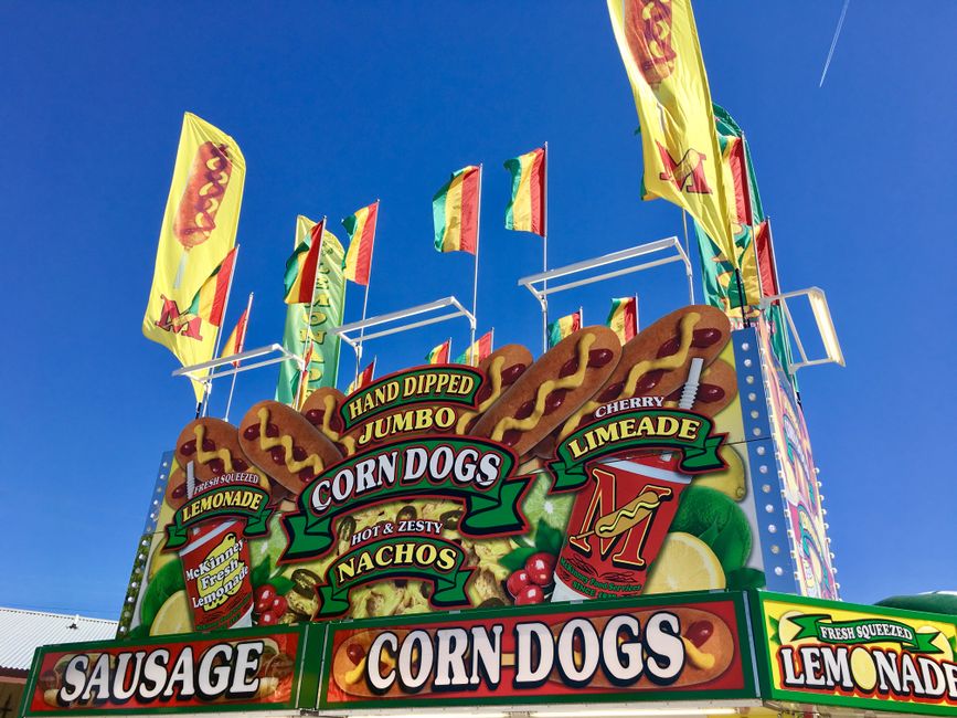 Vibrant fair stand in Grapevine, TX with corn dogs, lemonade, and flags under clear skies.