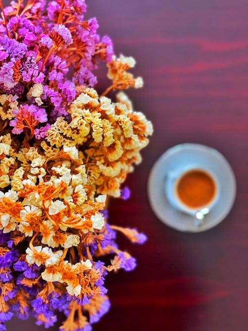 Colorful Flowers on a Vase Beside a Cup of Coffee