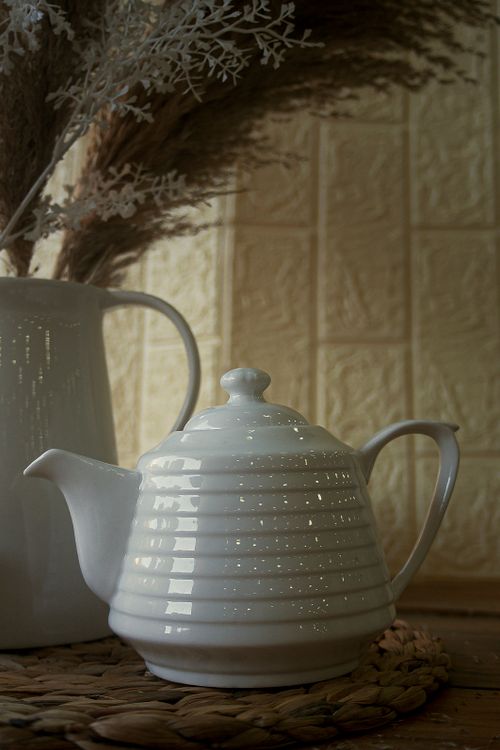 Free A close-up of a white ceramic teapot with a textured background, ideal for kitchen decor visuals. Stock Photo