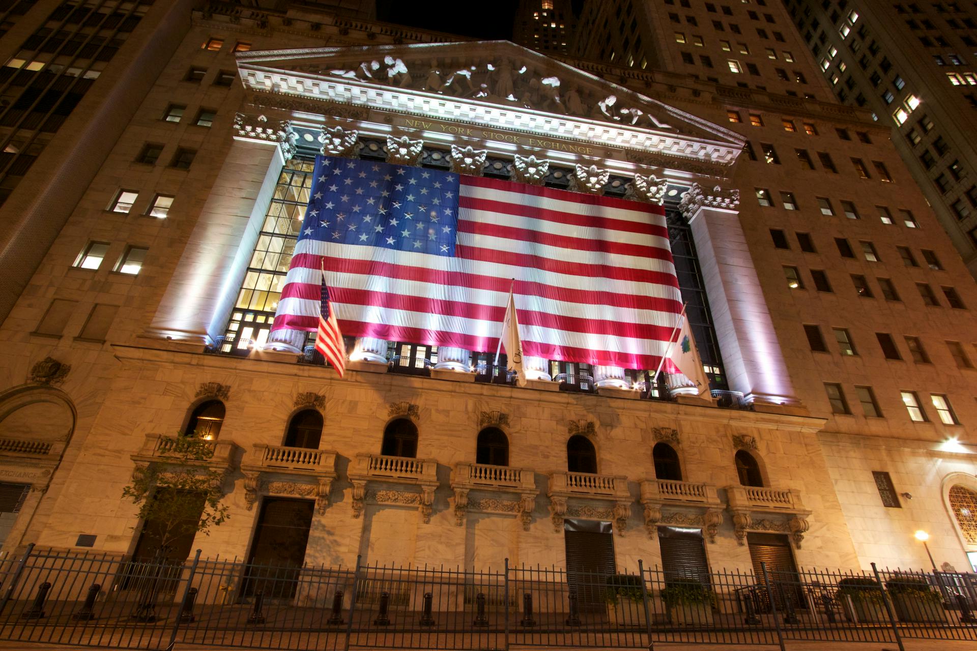 A nighttime view of the New York Stock Exchange with an American flag displayed prominently.