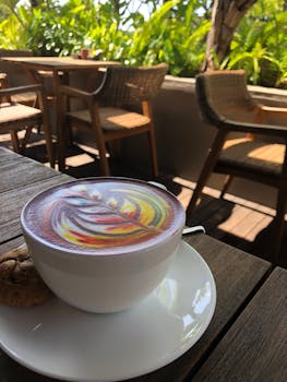 户外木桌上，白色杯中的彩虹拿铁艺术和饼干生动地摆放着