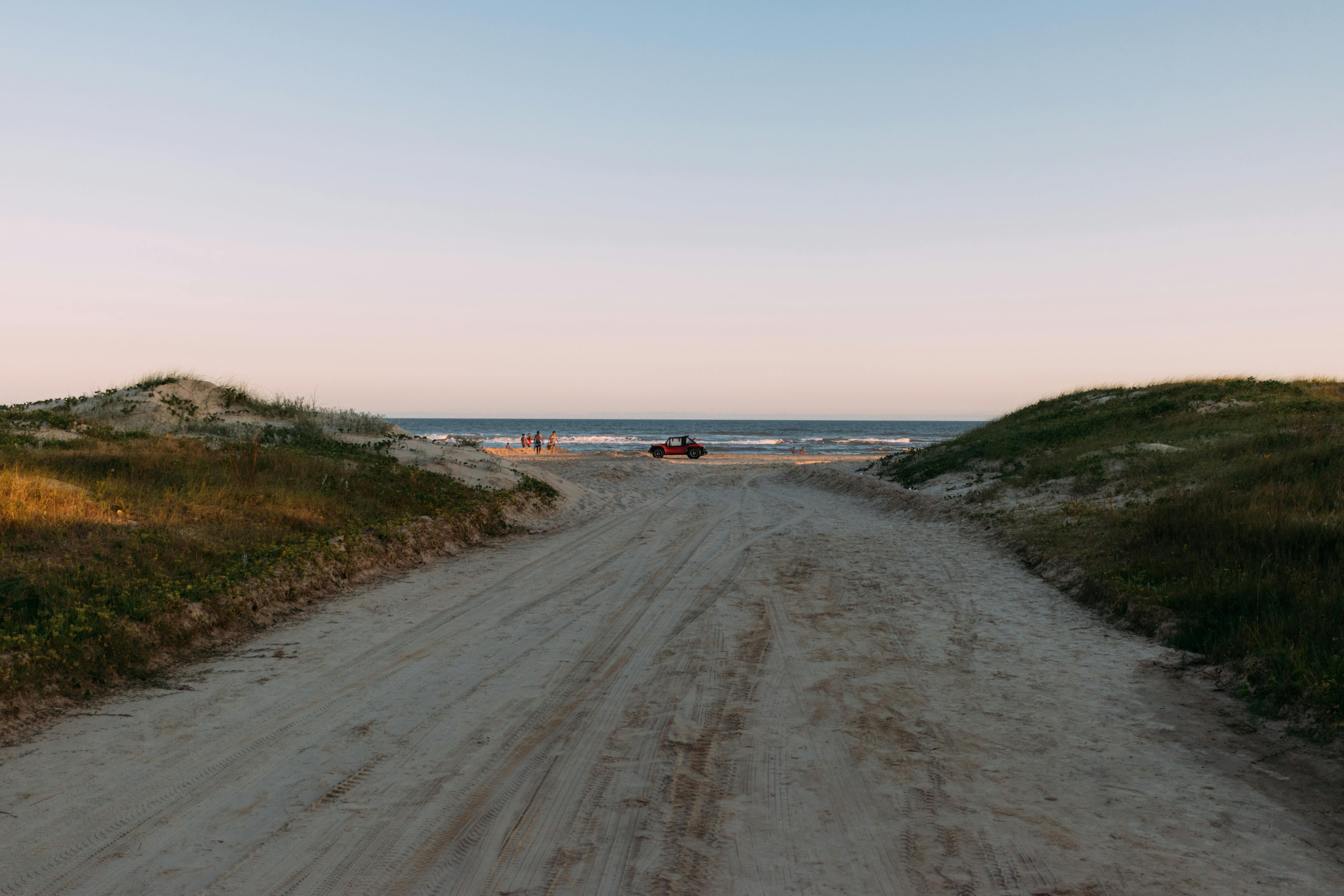 A sandy path leading to the ocean surrounded by gentle dunes and a setting sun at Arroio do Silva, Brazil.