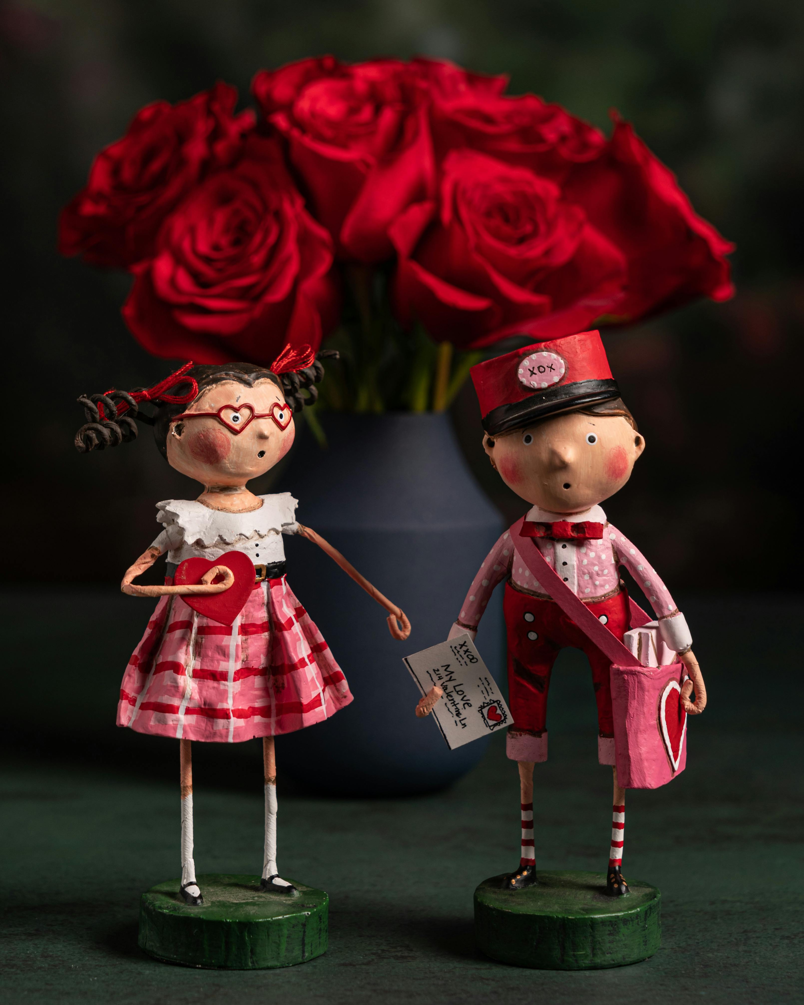 a boy and a girl miniatures beside a bouquet of red roses