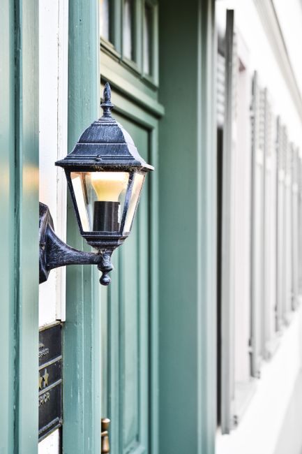 A close-up of a vintage wall sconce on a green modern building facade with shutter details.