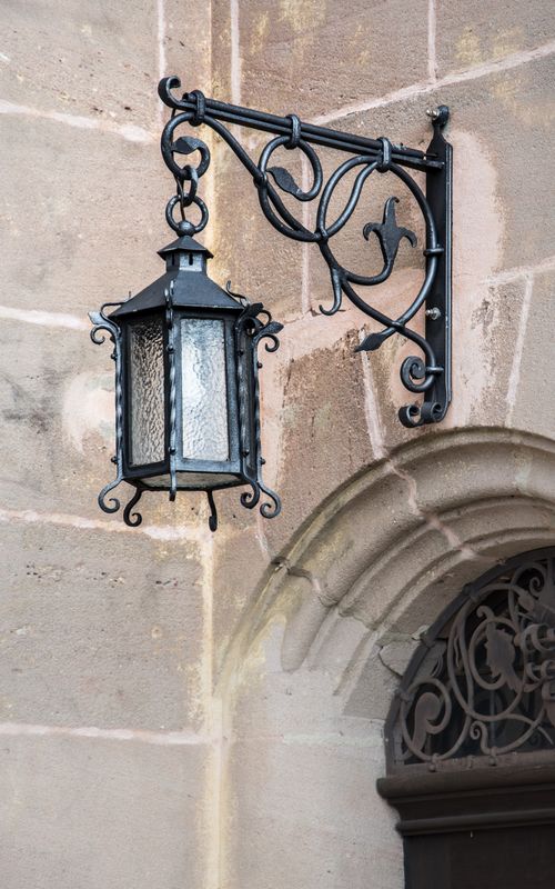 Free Ornate iron lantern mounted on a rustic stone wall, classic architectural detail. Stock Photo