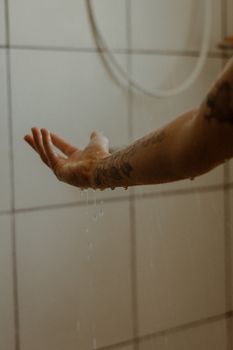 A tattooed arm extends to catch water droplets in a serene indoor setting.