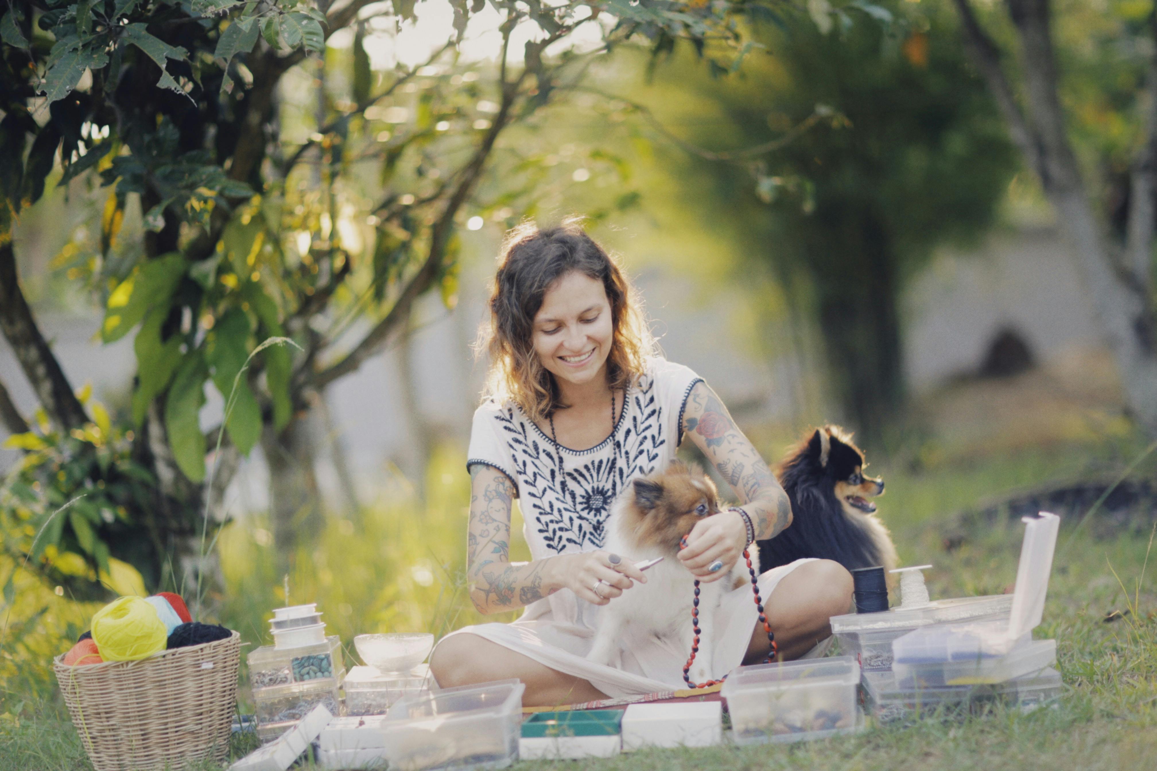 woman in park making jewelry with her dogs sitting next to her