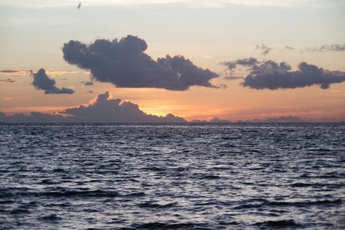 Free Captivating ocean view at sunset with dramatic clouds and golden hour lighting. Stock Photo