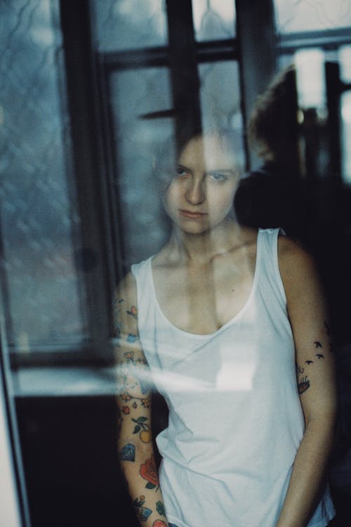 Woman in White Tank Top Standing Behind Glass