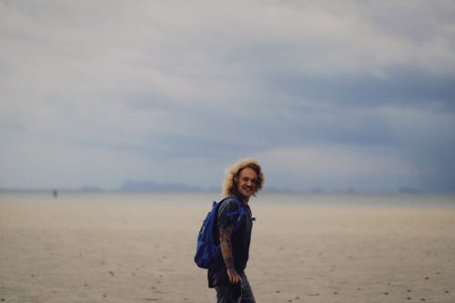 Free A man smiling while walking on a vast sandy beach under a cloudy sky. Stock Photo