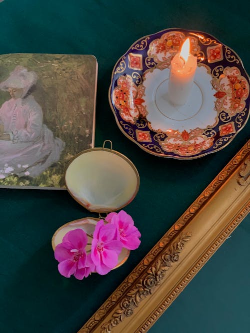 A Burning Candle, a Painting and Flowers on a Table 