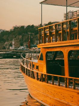 A classic wooden boat docked against a sunset backdrop with modern cityscape in the background.