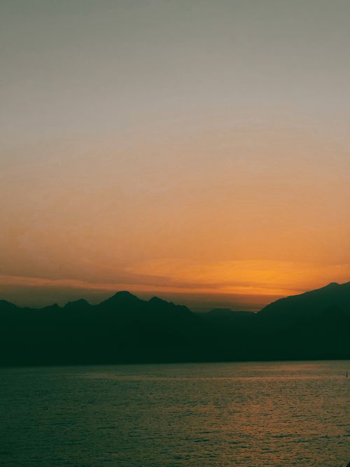 Free Beautiful sunset view with mountains silhouetted against a glowing sky over the ocean. Stock Photo