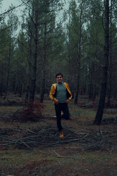 Free Caucasian man wearing a yellow jacket strolling through a serene forest. Stock Photo