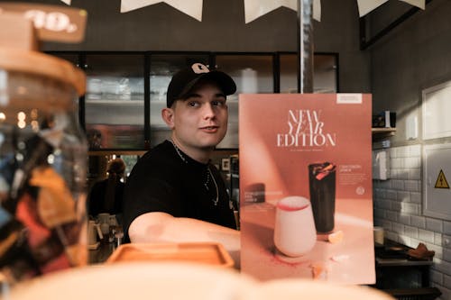 Man Wearing a Cap Sitting at a Cafe Table with Pink Menu