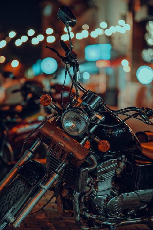 Free A classic motorcycle illuminated by city lights in an urban night scene. Stock Photo